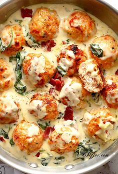 a pan filled with meatballs covered in cheese and spinach garnished with sauce