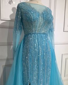 a blue dress with sequins on the shoulders and long sleeves is displayed in front of a white wall