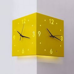 a yellow square clock with numbers on the face and hands is illuminated by a dim light