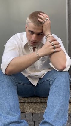 a man sitting on top of a wooden bench next to a wall with his hands in his hair