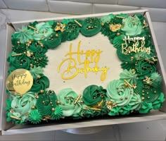 a birthday cake with green frosting and gold decorations in a box on a table