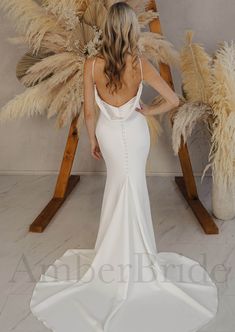 a woman in a white wedding dress standing next to tall pamodia plants and looking at the back of her gown