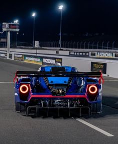 the rear end of a blue sports car driving on a race track at night time