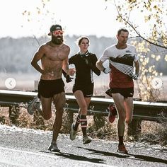 three shirtless men running in the road with trees and bushes behind them on a sunny day