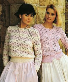 two women standing next to each other in front of a stone wall wearing sweaters and skirts