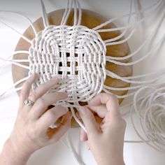 two hands are working on an object made out of white string and wood, while another hand is holding something in front of it