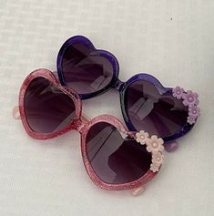 These heart-shaped glitter sunglasses measure 13 cm from ear to ear and 4.5 from top to bottom. The frame is made of plastic and the lenses are plastic as well. Heart-shaped Sunglasses With Heart Print For Party, Cute Party Sunglasses With Heart Print, Cute Heart Print Sunglasses For Party, Heart-shaped Party Sunglasses With Heart Print, Heart-shaped Multicolor Sunglasses With Gradient Lenses, Multicolor Heart-shaped Sunglasses With Gradient Lenses, Purple Plastic Party Sunglasses, Plastic Sunglasses With Uva Protection For Party, Fun Party Sunglasses With Heart Print