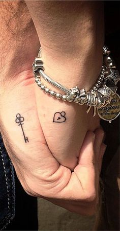 two people holding hands with tattoos on their fingers and one has a key to each other