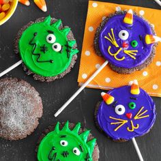 three decorated cupcakes with green and purple frosting on sticks in front of them