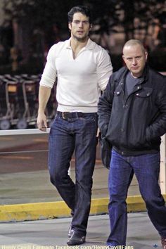 two men are walking down the street with one man in white shirt and blue jeans