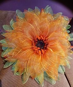 an orange flower with green leaves on it's center piece, sitting on a brown surface