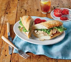 a chicken salad sandwich on a plate next to a glass of tomato juice and fork