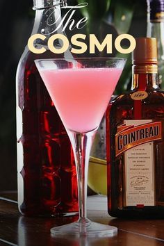 a bottle of cosmo sitting next to a glass filled with pink liquid and a drink