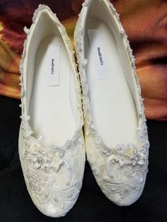 pair of white wedding shoes with flowers and pearls on the bottom, sitting on a black surface