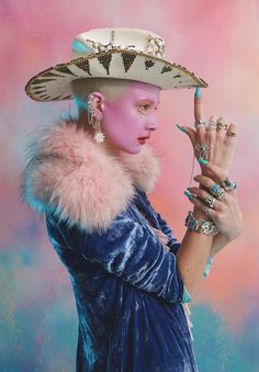 a woman in a blue dress and hat with her hand up to the side while wearing jewelry