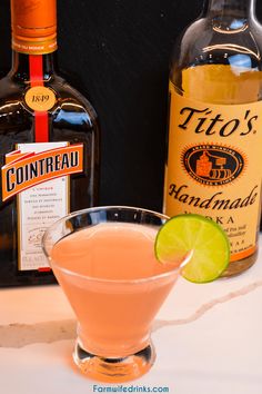 an alcoholic drink with a lime wedge in front of two bottles