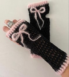 a hand holding a black and white knitted mitt with pink lace on it