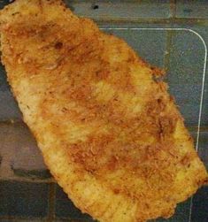 a piece of fried fish sitting on top of a metal rack in front of a brick wall