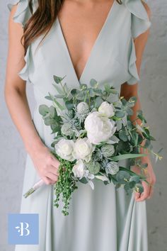 a woman in a blue dress holding a white bouquet with greenery and flowers on it