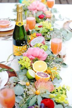 a long table with flowers, fruit and wine bottles on it is set up for a party