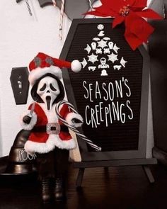 a santa clause doll sitting on top of a bell next to a sign that says season's greetings