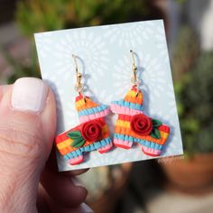 a person holding up a pair of earrings made out of paper and colored strips with flowers on them