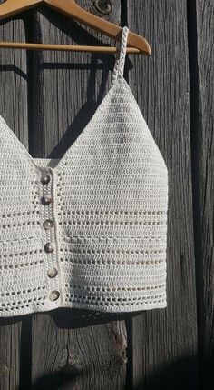 a white crocheted bra hanging on a wooden fence with a hanger in front of it