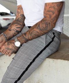 a man with tattoos is sitting on a ledge and has his hands in his pockets