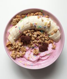 a pink bowl filled with yogurt, granola and a banana on top