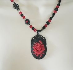 "Red Rose Necklace This beautiful necklace has red glass beads, black glass beads, seed beads, black metal connectors with rhinestones, black metal chain and a black metal pendant with resin rose. 20\" long. Lobster clasp." Gothic Beaded Necklace For Gift, Black Necklace With Rose Design As Gift, Black Necklace With Rose Design For Gift, Gothic Black Bead Necklace For Gift, Gothic Black Beads Necklace For Gift, Handmade Red Victorian Necklace, Red Handmade Victorian Necklace, Handmade Victorian Red Necklace, Gothic Choker Necklace