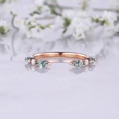 an image of a rose gold ring with green stones on it and flowers in the background