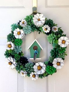 a wreath with flowers and a birdhouse hanging on the front door to decorate it