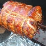 a large piece of meat is being cooked on an outdoor grill with foil wrapped around it