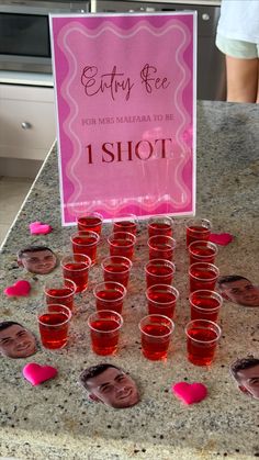 a table topped with lots of cups filled with red liquid next to a pink sign