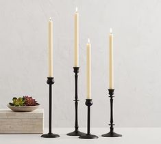 four candles are lined up next to each other on a white table with a plant in the background