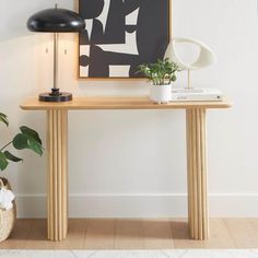 a wooden table topped with a lamp next to a potted plant and a painting