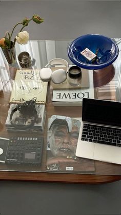 a laptop computer sitting on top of a glass table covered in books and other items