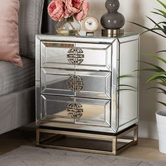 a mirrored cabinet with two drawers and flowers on the table next to it, in front of a gray couch