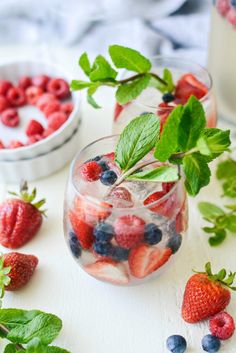 berries, mint and water in glasses on a white surface with strawberries and raspberries