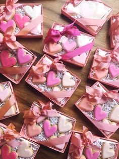 many pink and white heart shaped cookies in small boxes on a wooden table with ribbons