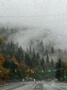 rain is falling on the street and cars are driving down the road with trees in the background