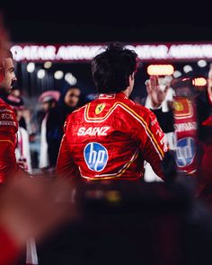 two men in red racing suits standing next to each other with their hands raised up