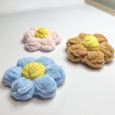 three different colored flower shaped hair clips on top of a white table with a mirror in the background