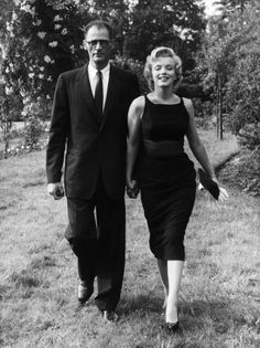 an old black and white photo of a man and woman walking together in the grass