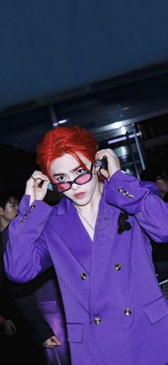 a woman with red hair wearing a purple suit and holding her hands to her ears