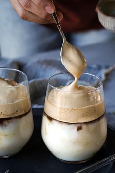 two glasses filled with ice cream on top of a black tray next to a spoon