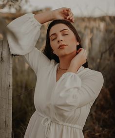 a woman in a white dress leaning against a fence