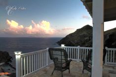 two chairs sitting on top of a patio next to the ocean at sunset with clouds in the sky