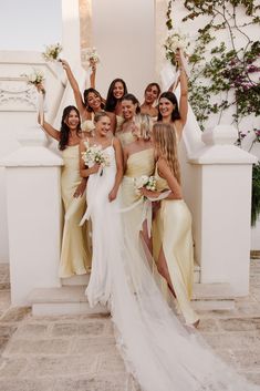 a group of women standing next to each other in front of a white wall holding bouquets