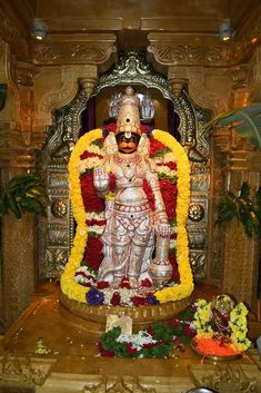 the statue is surrounded by flowers and other items in front of it, including an idol